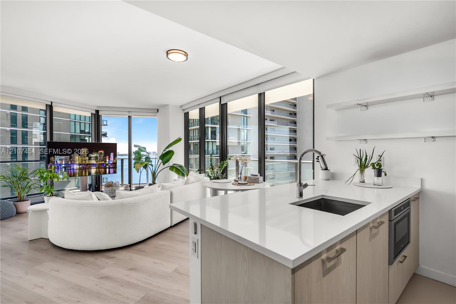 Kitchen featuring a white quartz countertop, undermount sink, gooseneck faucet, light-finish cabinetry, and built-in microwave, complemented by wood-finish flooring and floor-to-ceiling windows