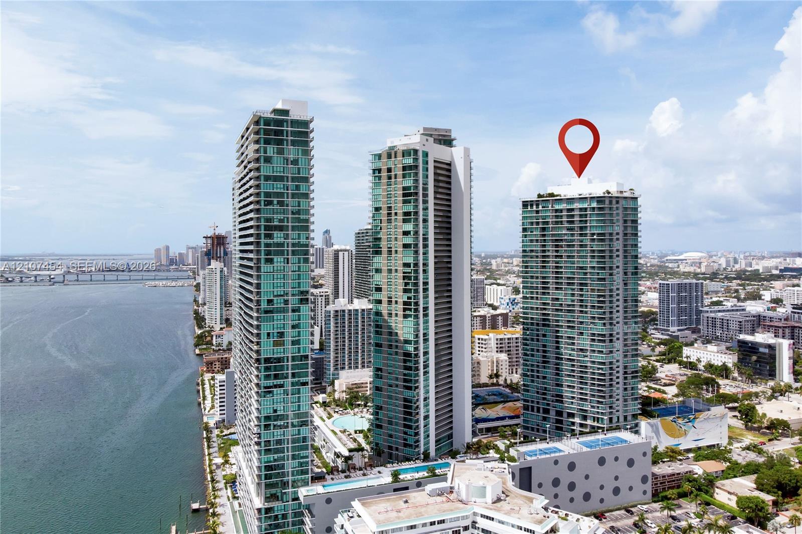 High-rise glass facade condominium tower featuring private balconies, integrated parking structure, and rooftop amenity deck, situated within a coastal urban environment