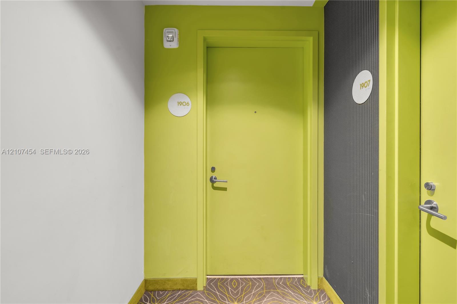 Entryway featuring lime green doors with brushed metal hardware, circular unit signage, and textured dark grey wall paneling
