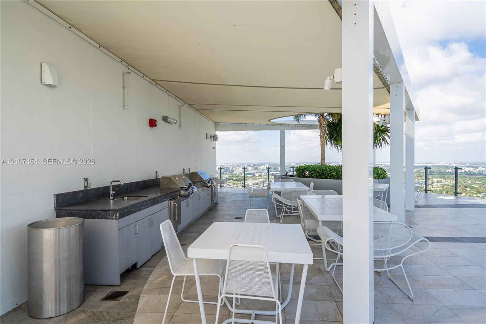 Covered outdoor terrace featuring a built-in kitchen, dark stone countertop, integrated stainless steel appliances, and metal railing