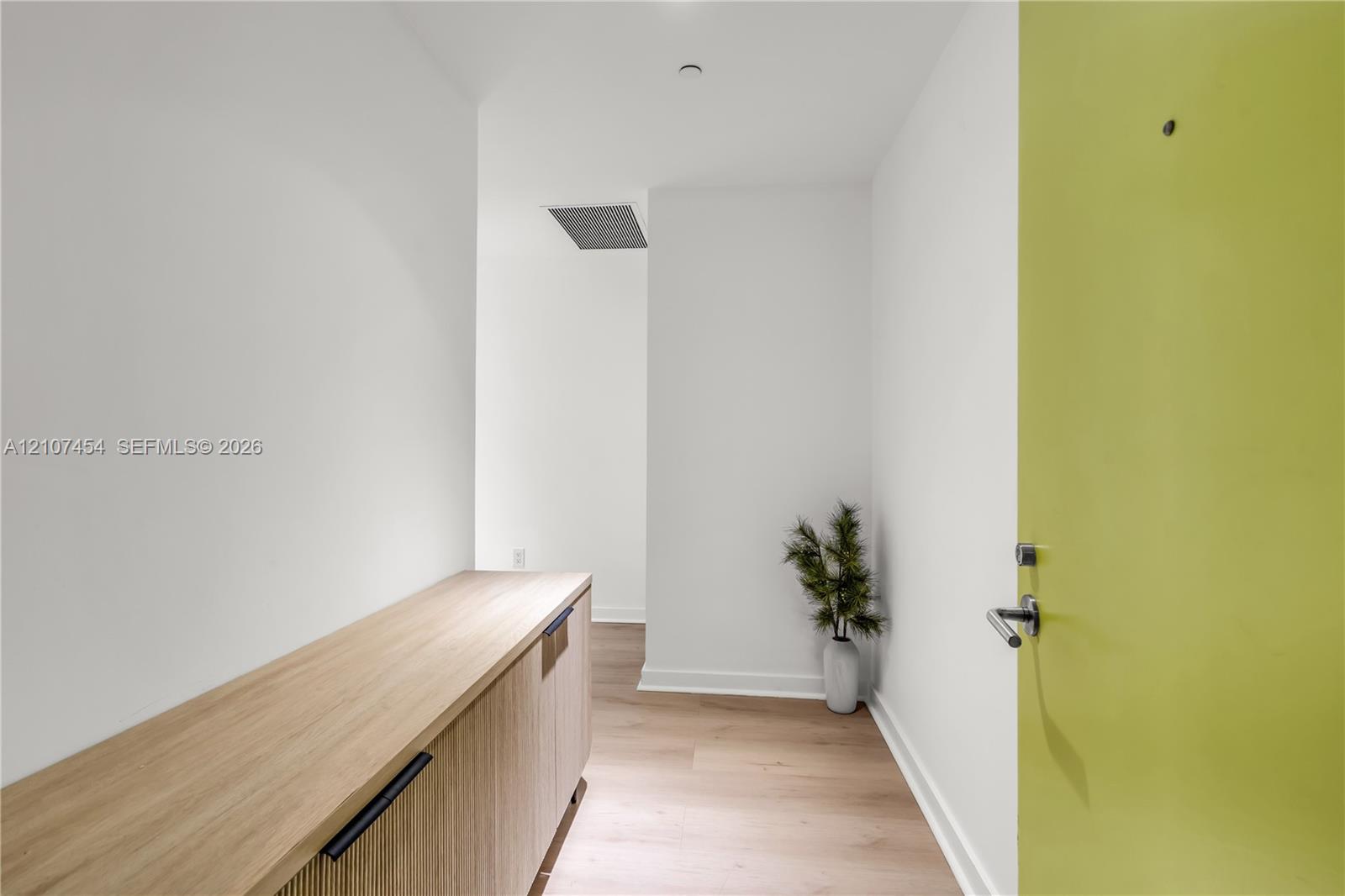 Entryway featuring a light-tone door with a modern lever handle, built-in wooden cabinetry with matte black hardware, and light wood-finish flooring