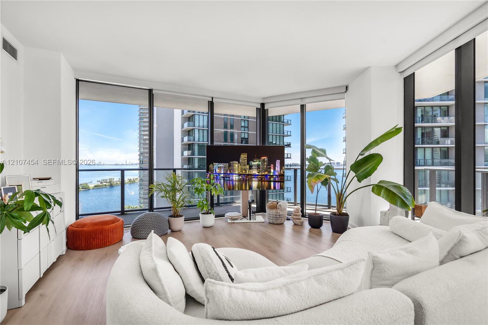 Floor-to-ceiling windows, wood-finish flooring, and black metal-framed balcony access with a glass railing