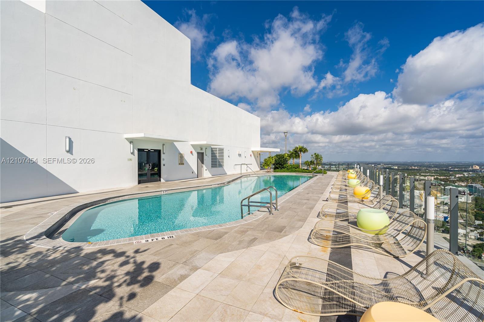 Rooftop swimming pool featuring stone tile decking, perimeter glass railing, and metal handrails
