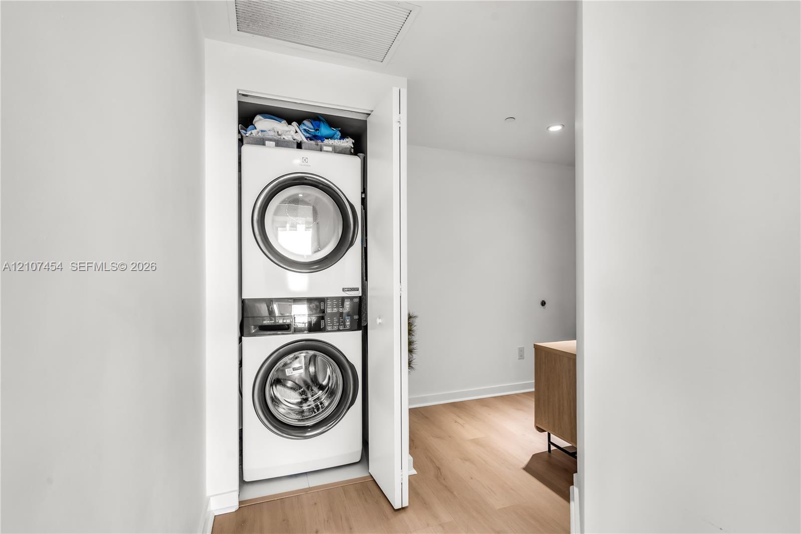 Stacked front-loading washer and dryer unit enclosed in a dedicated closet featuring light wood-finish flooring