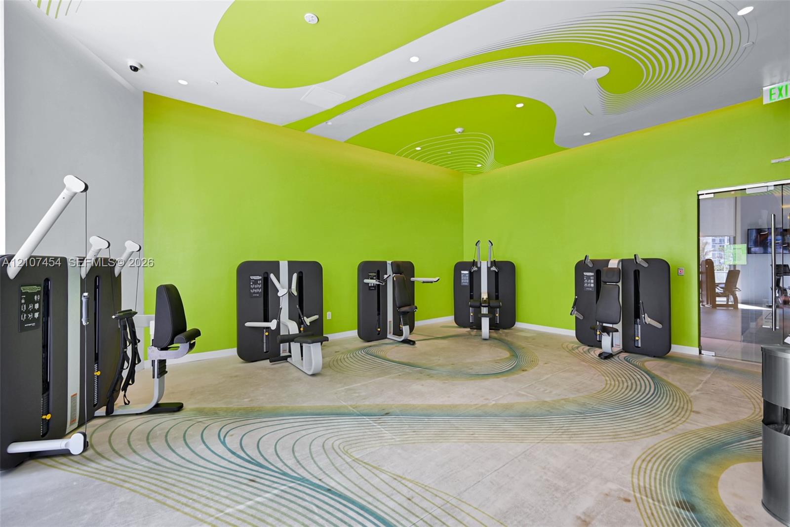 Fitness center featuring polished concrete flooring with a decorative inlay pattern, high ceilings with stylized graphic accents, and recessed lighting