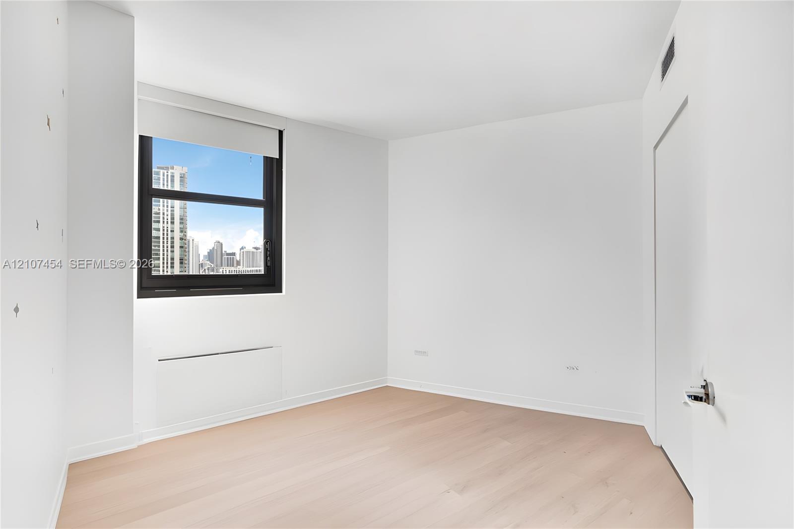 Light-filled interior featuring wood-finish flooring, a large window with urban skyline exposure, and clean, neutral wall finishes
