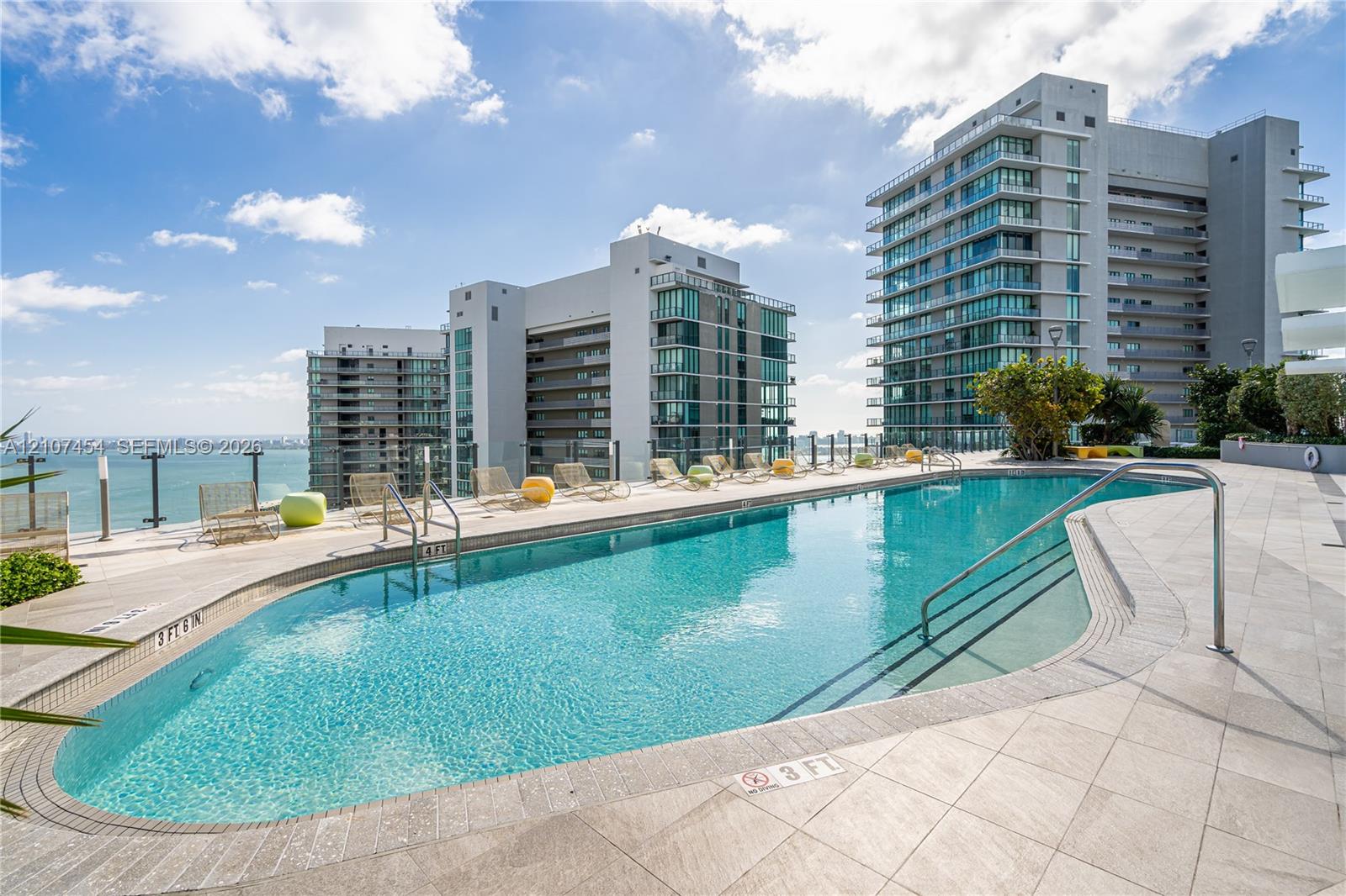 Curved swimming pool featuring a tile surround, metal handrails, and a glass panel perimeter fence