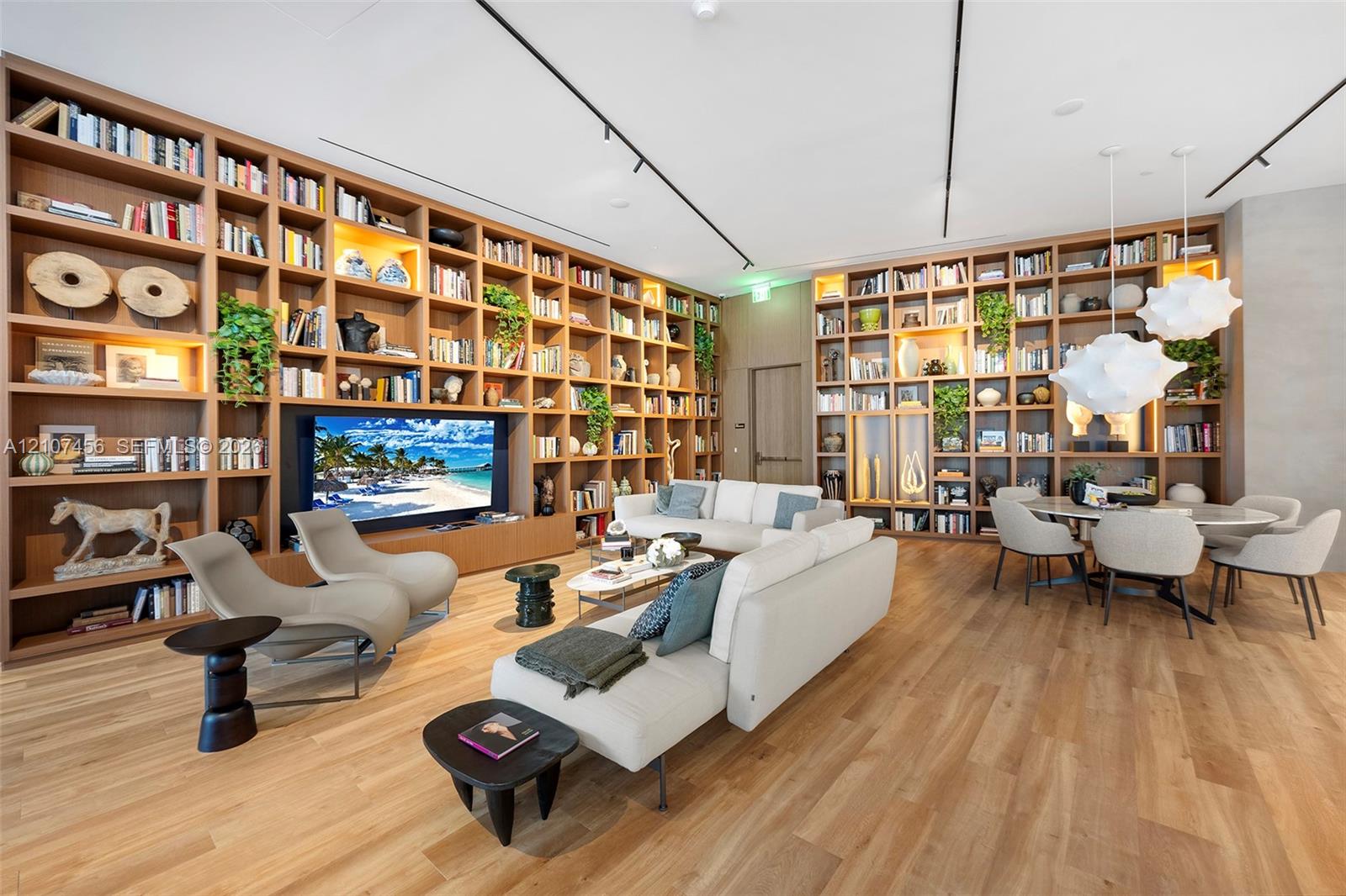 Floor-to-ceiling custom wood-finish built-in shelving, integrated track lighting, wood-finish flooring, and sculptural pendant lighting