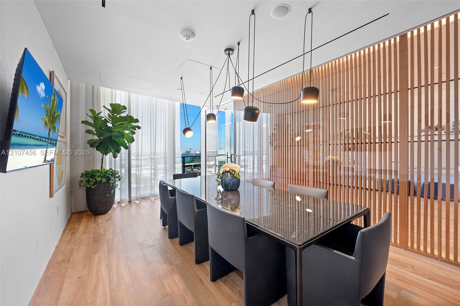 Floor-to-ceiling windows, wood-finish flooring, decorative vertical slat room divider, and multi-pendant architectural lighting