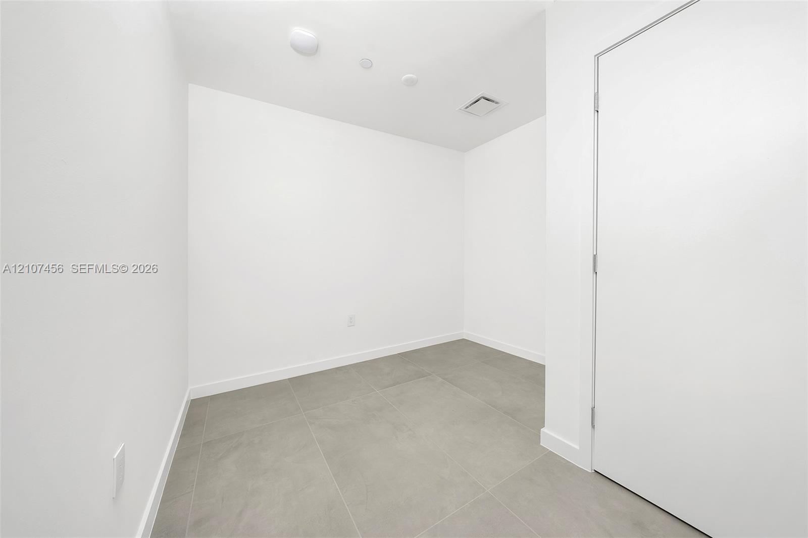 Interior room featuring neutral wall paint, large-format grey tile flooring, and a single-panel interior door