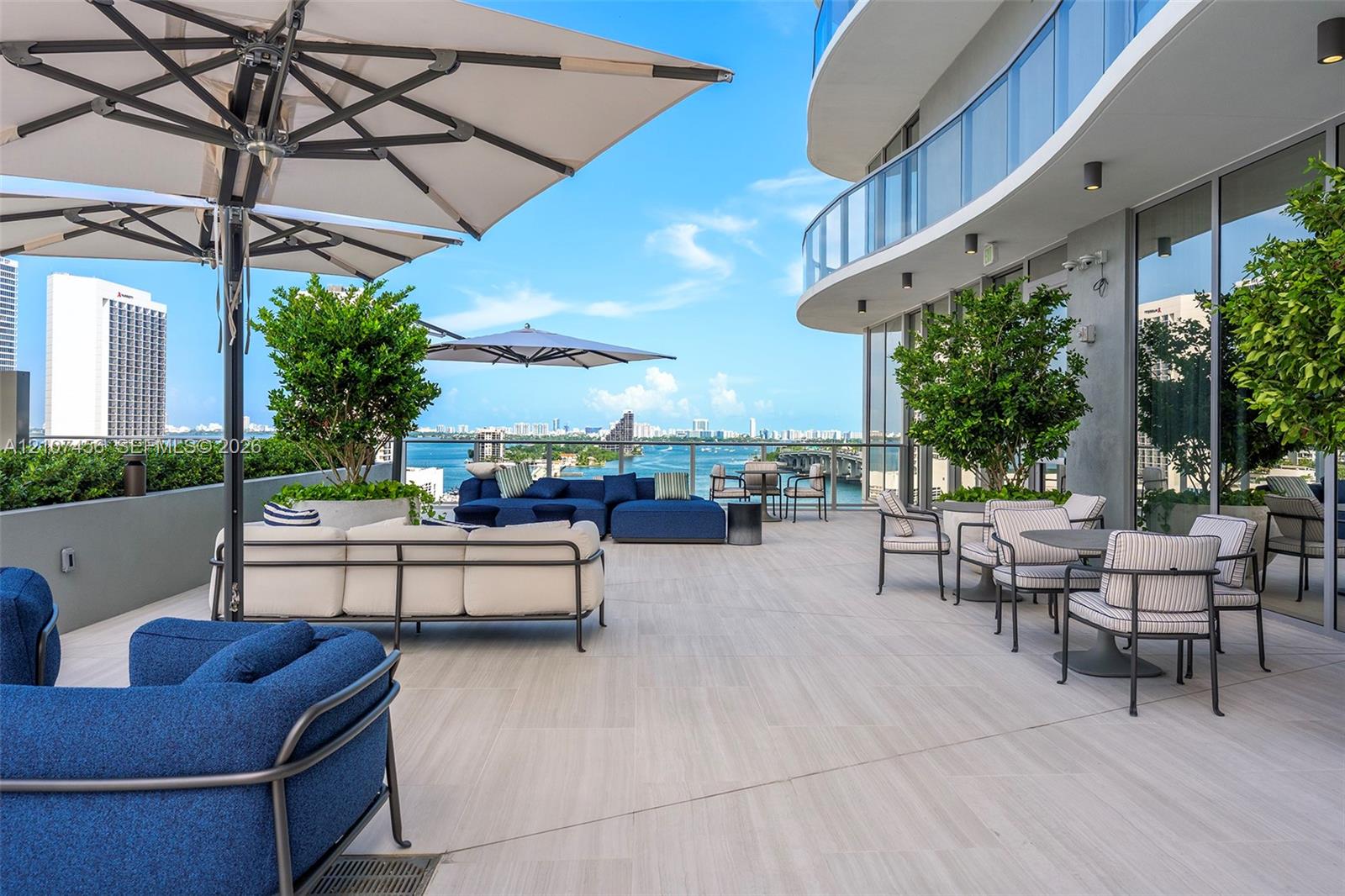 Expansive wraparound balcony featuring large-format tile flooring, a glass-panel railing, integrated wall-mounted lighting, and built-in landscape planters