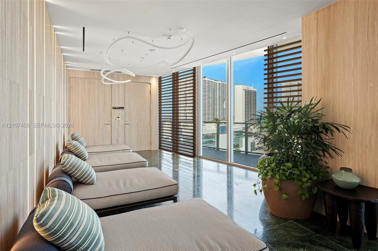 Floor-to-ceiling windows with horizontal louvered screens, natural wood-finish wall paneling, integrated recessed LED accent lighting, contemporary sculptural overhead light fixture, and polished stone flooring