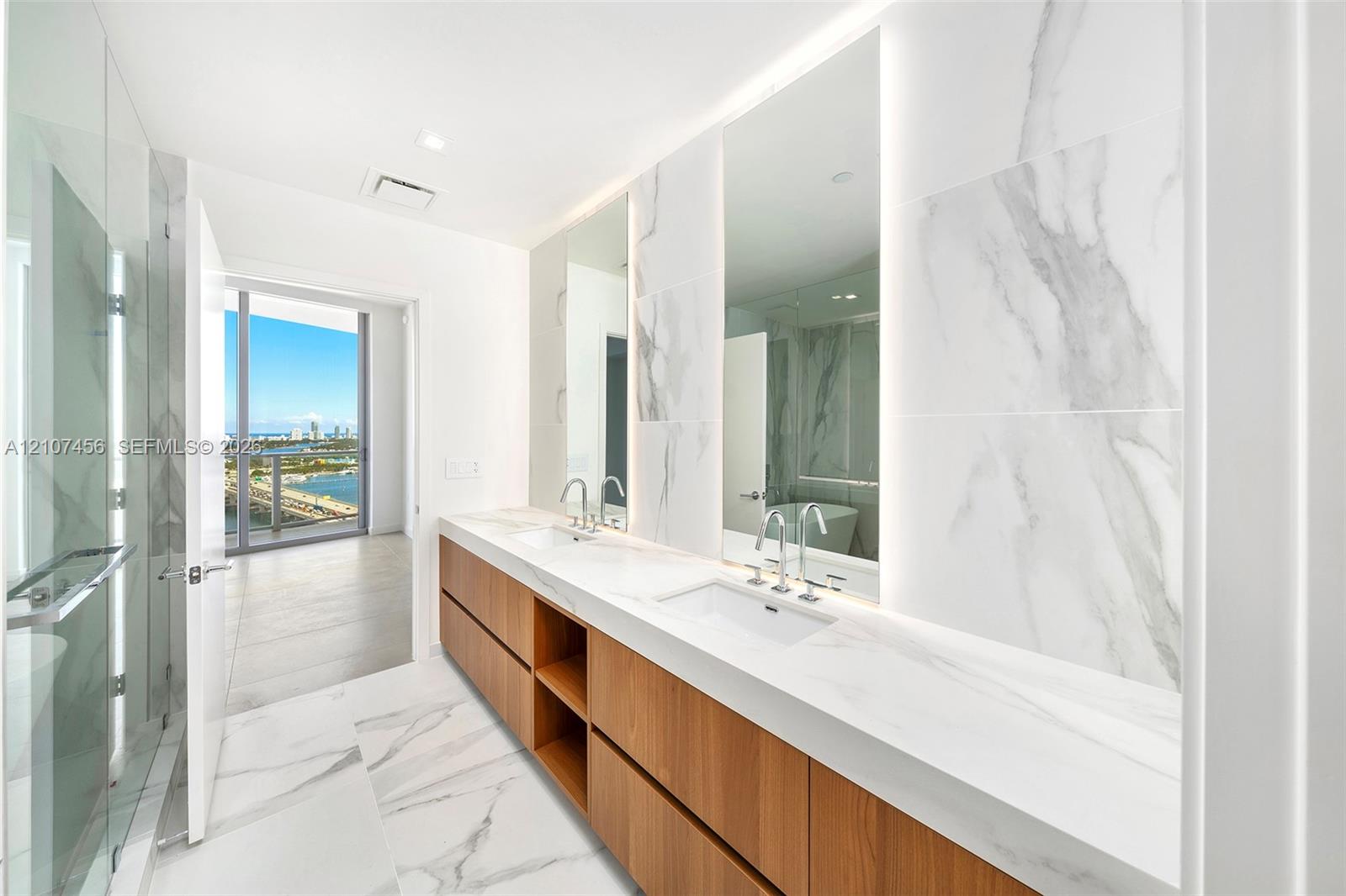 Dual-sink vanity with wood-finish cabinetry, solid surface countertops, floor-to-ceiling porcelain tile, integrated LED-lit mirrors, and a glass-enclosed shower