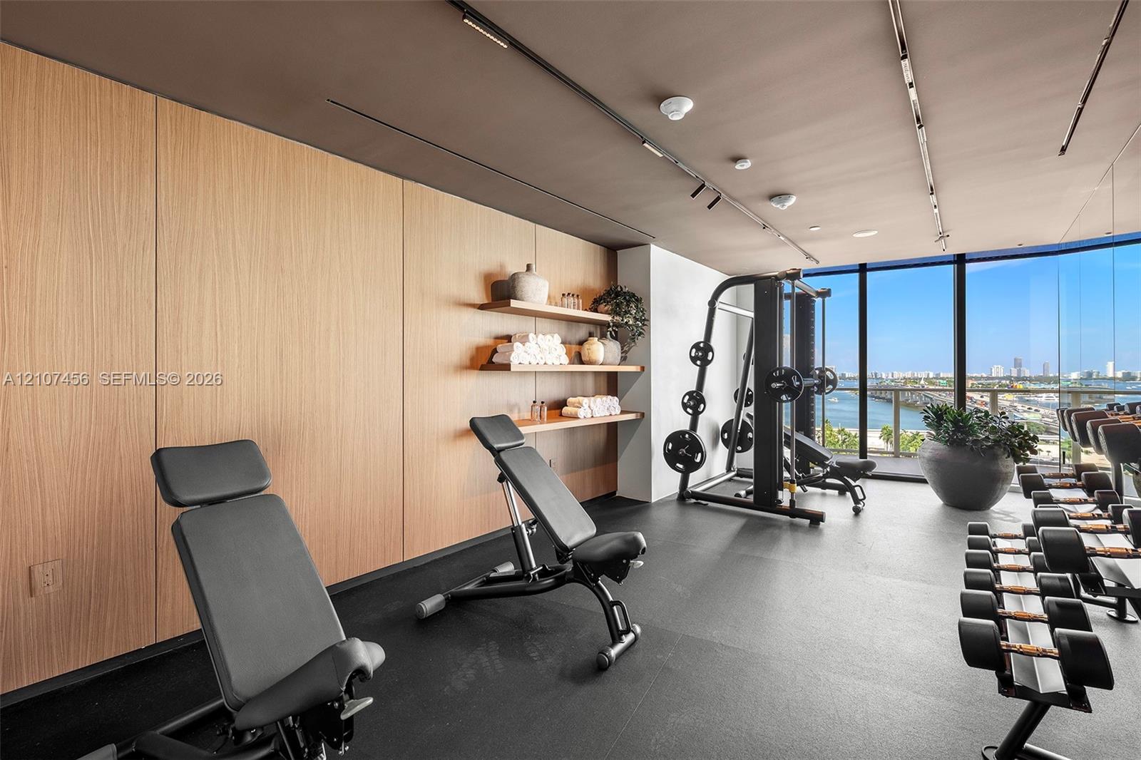 Floor-to-ceiling windows, wood-panelled accent wall, built-in open shelving, track lighting, and rubberized flooring