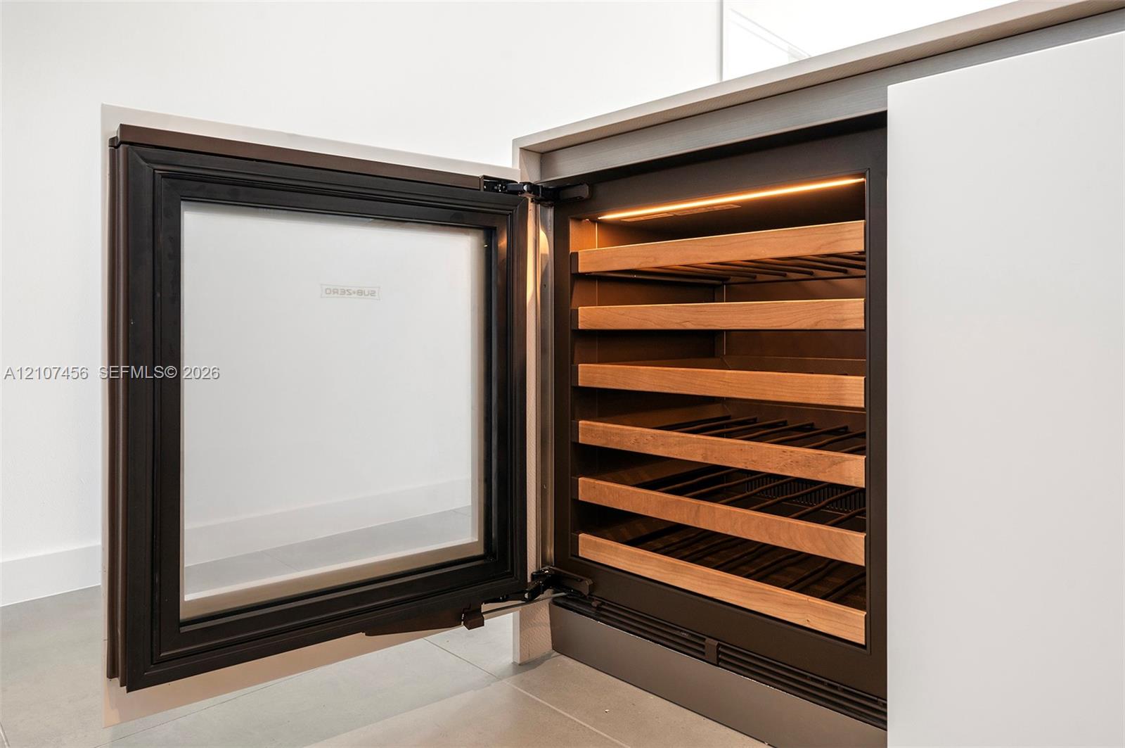 Built-in under-counter beverage refrigerator featuring a glass door, matte black frame, integrated internal lighting, and horizontal wood-finish shelving