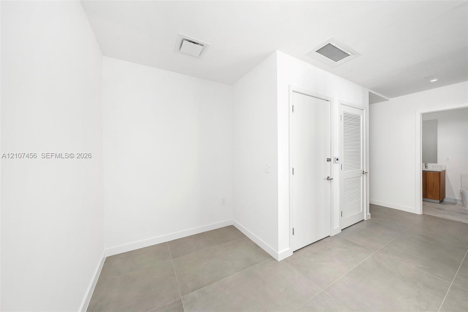 Interior space featuring large-format tile flooring, crisp white walls, solid-core interior doors, and a louvered closet door
