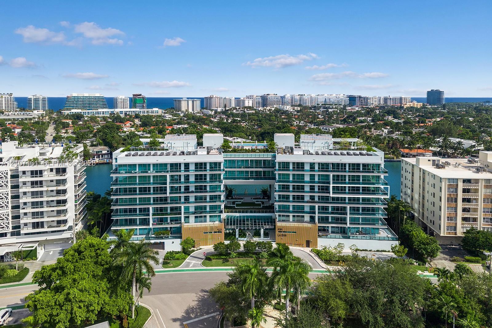 Mid-rise residential building featuring floor-to-ceiling glass windows, wraparound balconies, structured parking, and waterfront positioning