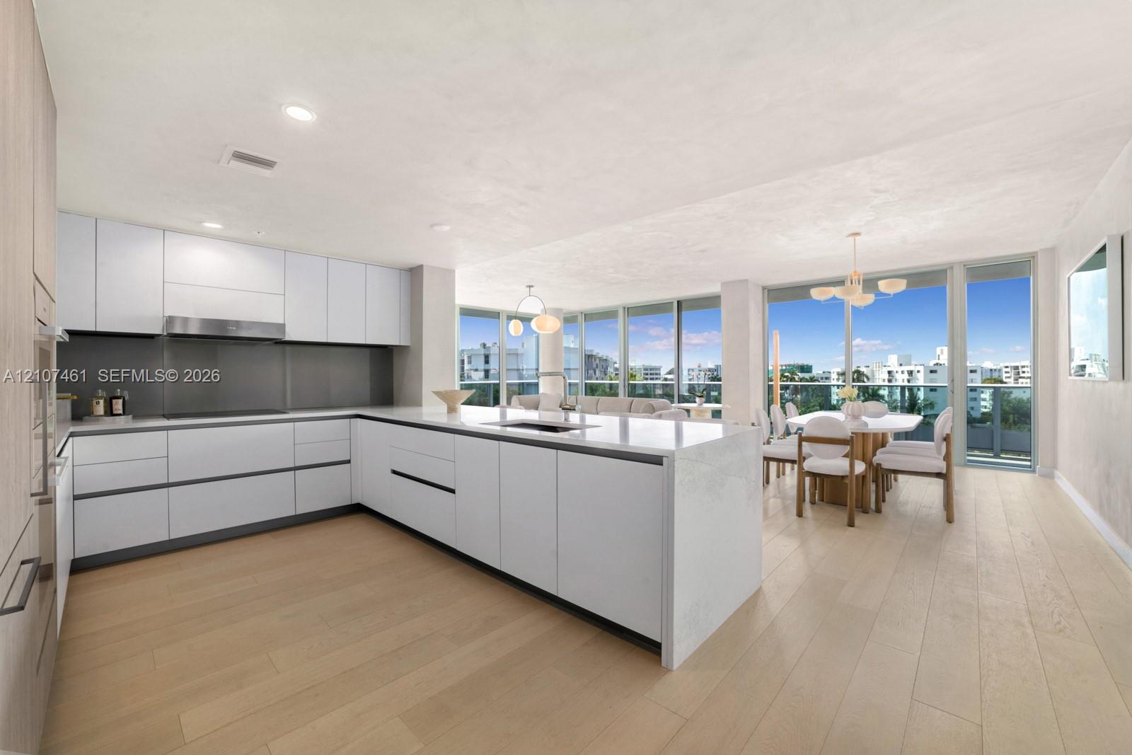 Contemporary kitchen featuring flat-panel cabinetry, a central island with a solid-surface countertop, recessed lighting, and expansive floor-to-ceiling windows