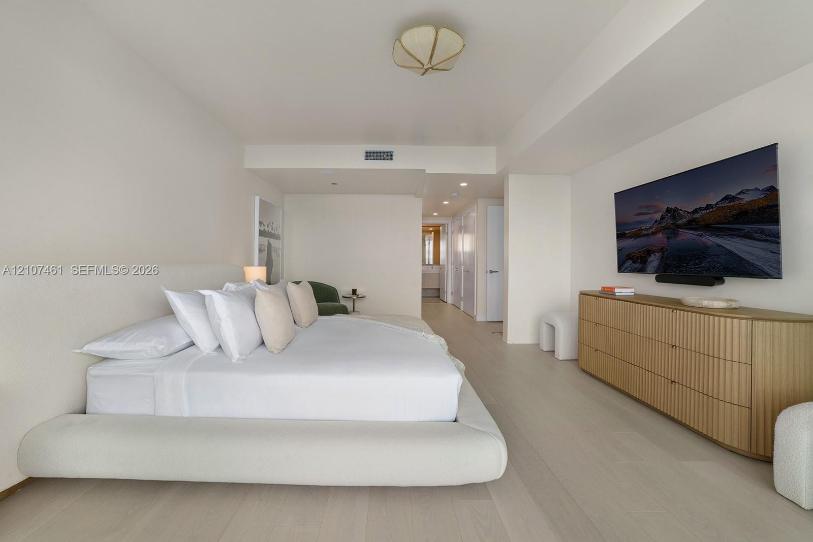 Spacious room featuring light-toned wood-finish flooring, recessed ceiling lighting, a sculpted semi-flush mount fixture, and smooth wall finishes