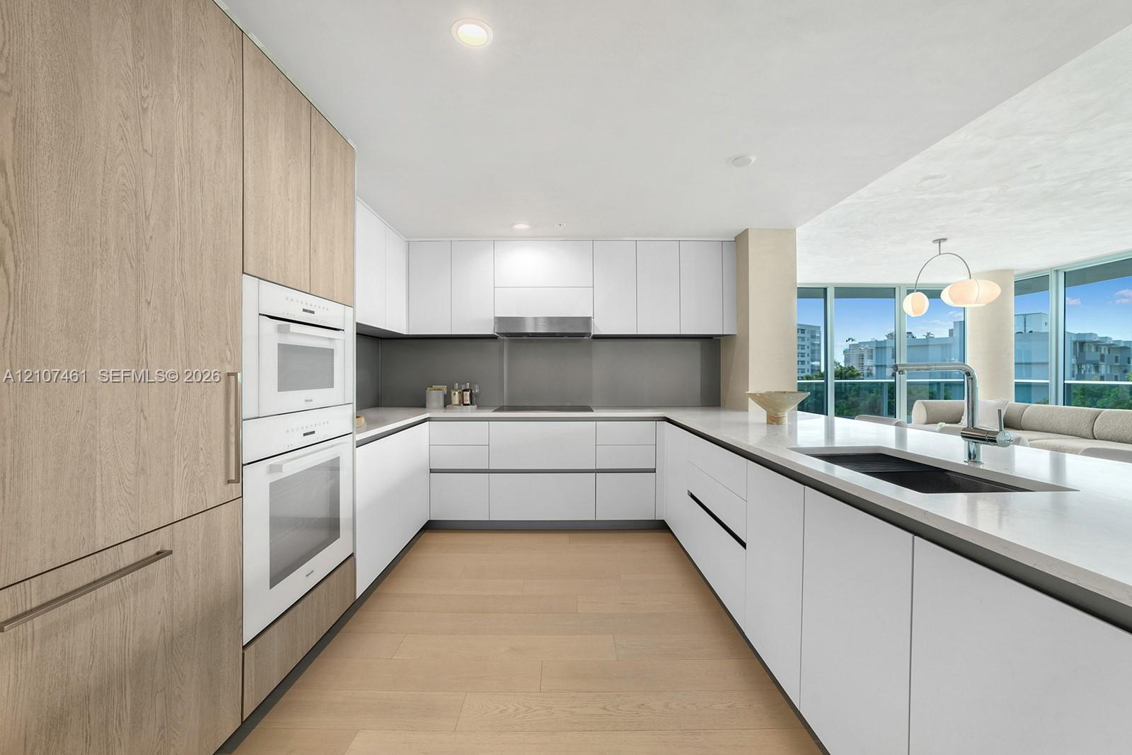 Modern kitchen featuring flat-panel cabinetry, light-toned wood-finish flooring, integrated wall ovens, solid-surface countertops, and recessed lighting
