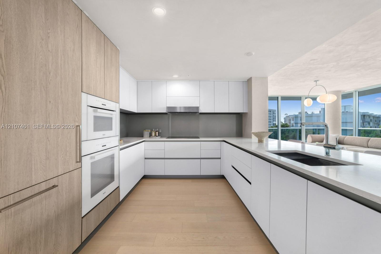 Kitchen featuring custom cabinetry, integrated double wall ovens, solid-surface countertops, floor-to-ceiling windows, and wood-finish flooring