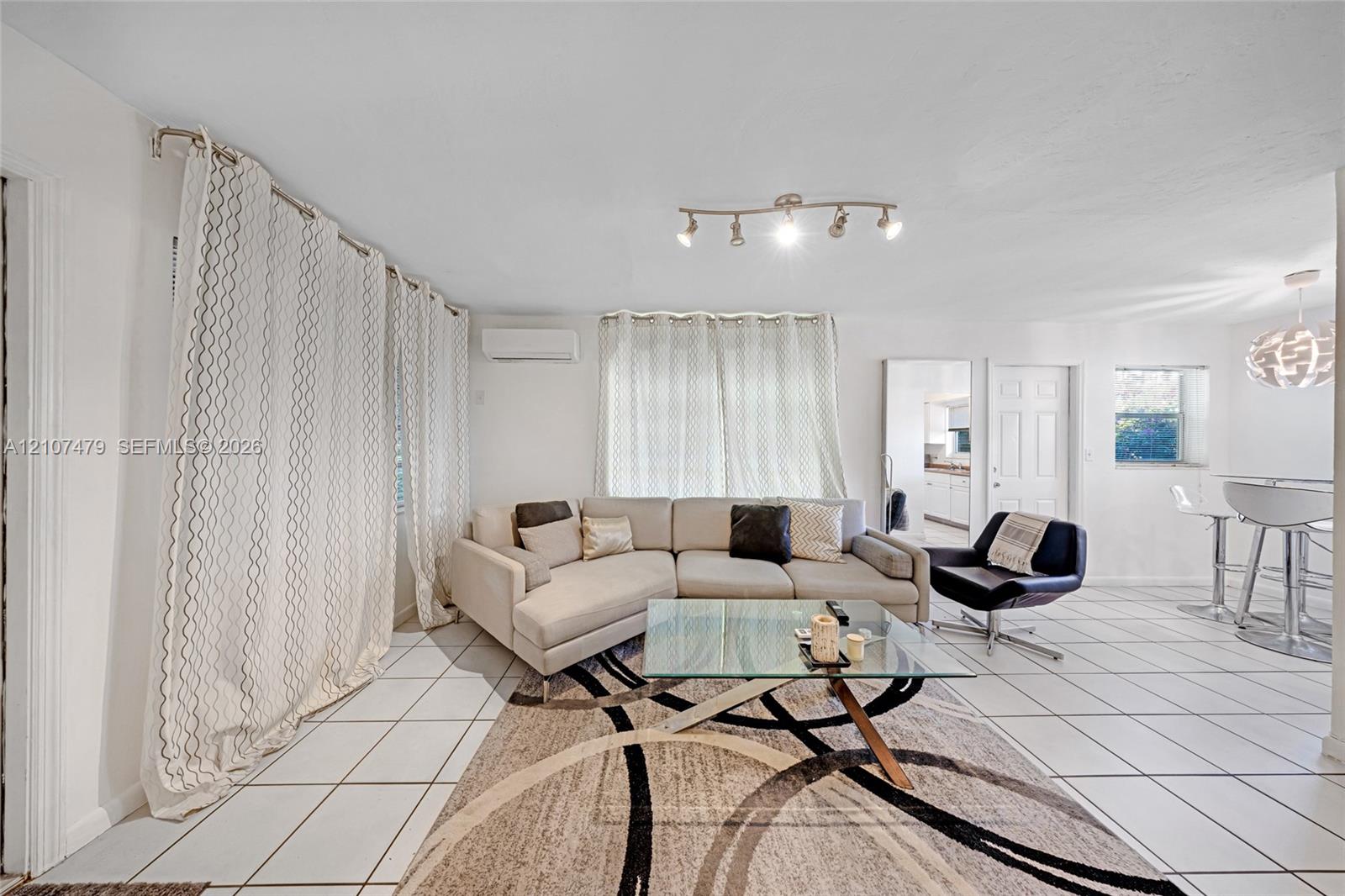 Open living area featuring large-format tile flooring, adjustable track lighting, and a wall-mounted ductless climate control unit