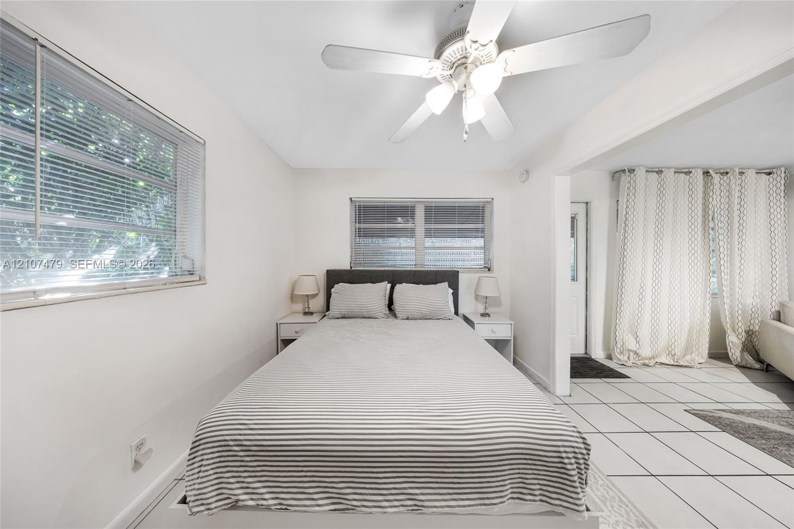 Neutral-toned room featuring a white ceiling fan with integrated lighting, dual horizontal windows, and large-format tile flooring