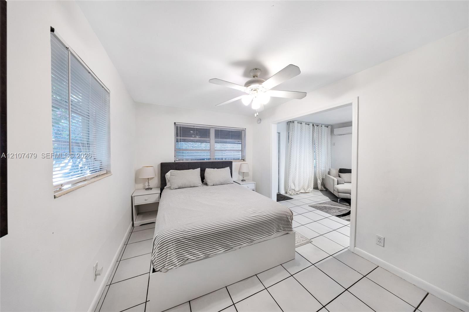 Interior space featuring large-format ceramic floor tiling, white walls, two windows with integrated blinds, and a central ceiling fan with integrated light fixture