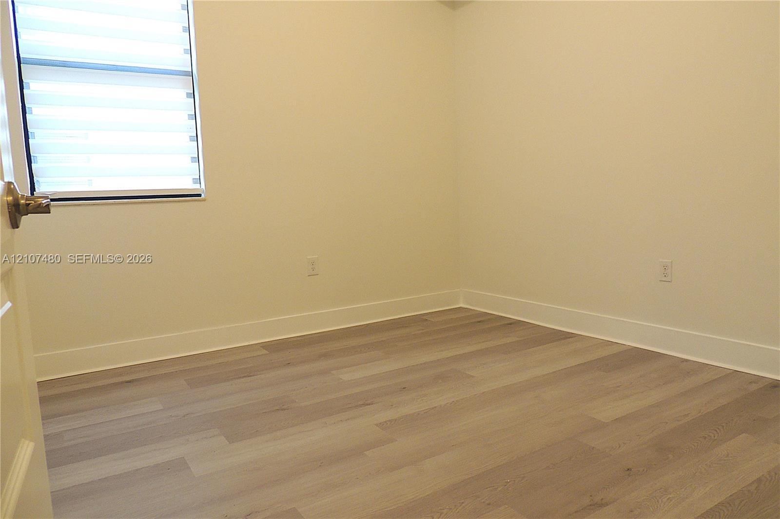 Wood-finish flooring, neutral wall tones, and a window fitted with horizontal blinds