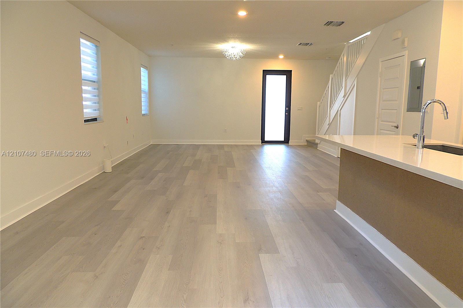 Open-concept interior featuring light wood-finish flooring, a kitchen island with stone-surface countertop, recessed lighting, and a staircase with decorative railing Open-concept interior featuring light wood-finish flooring, a kitchen island with stone-surface countertop, recessed lighting, and a staircase with decorative railing
