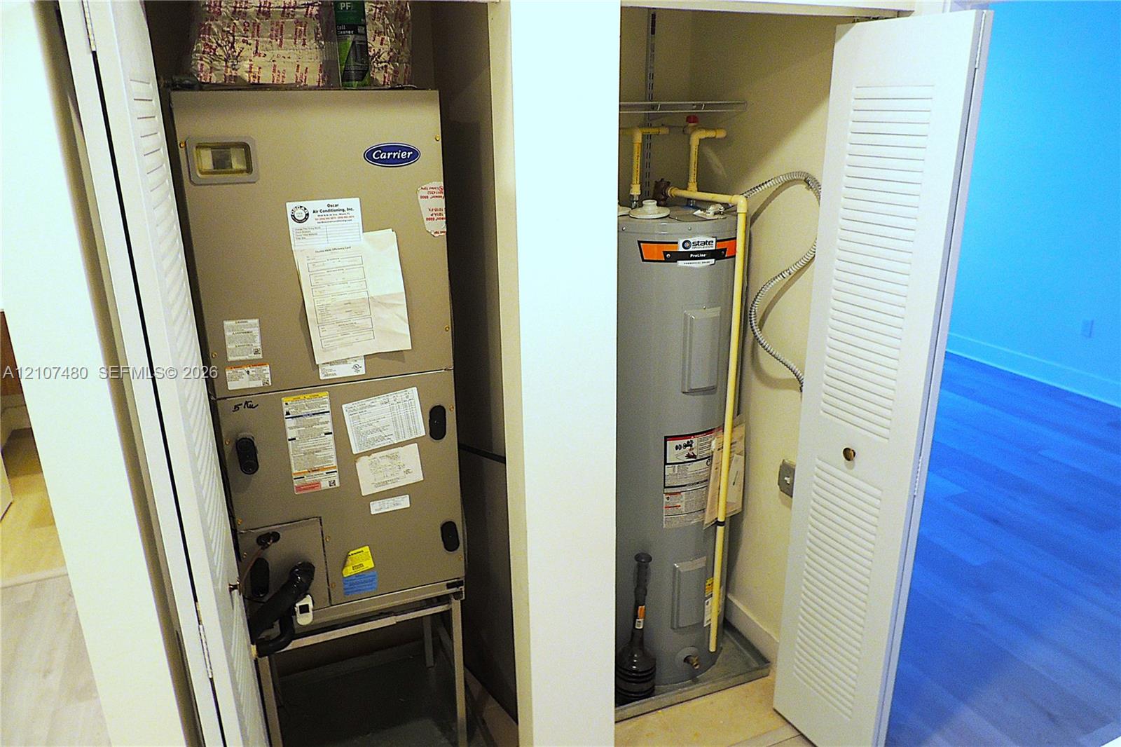 Utility closet containing a Carrier HVAC unit and a vertical water heater, enclosed by dual louvered doors
