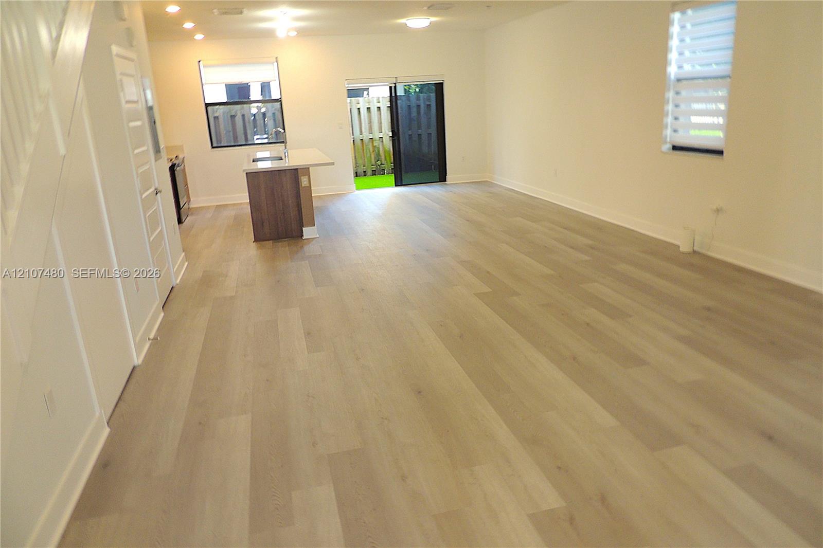 Open-concept floor plan featuring wood-finish flooring, recessed lighting, a center island with countertop seating, and sliding glass doors Open-concept floor plan featuring wood-finish flooring, recessed lighting, a center island with countertop seating, and sliding glass doors