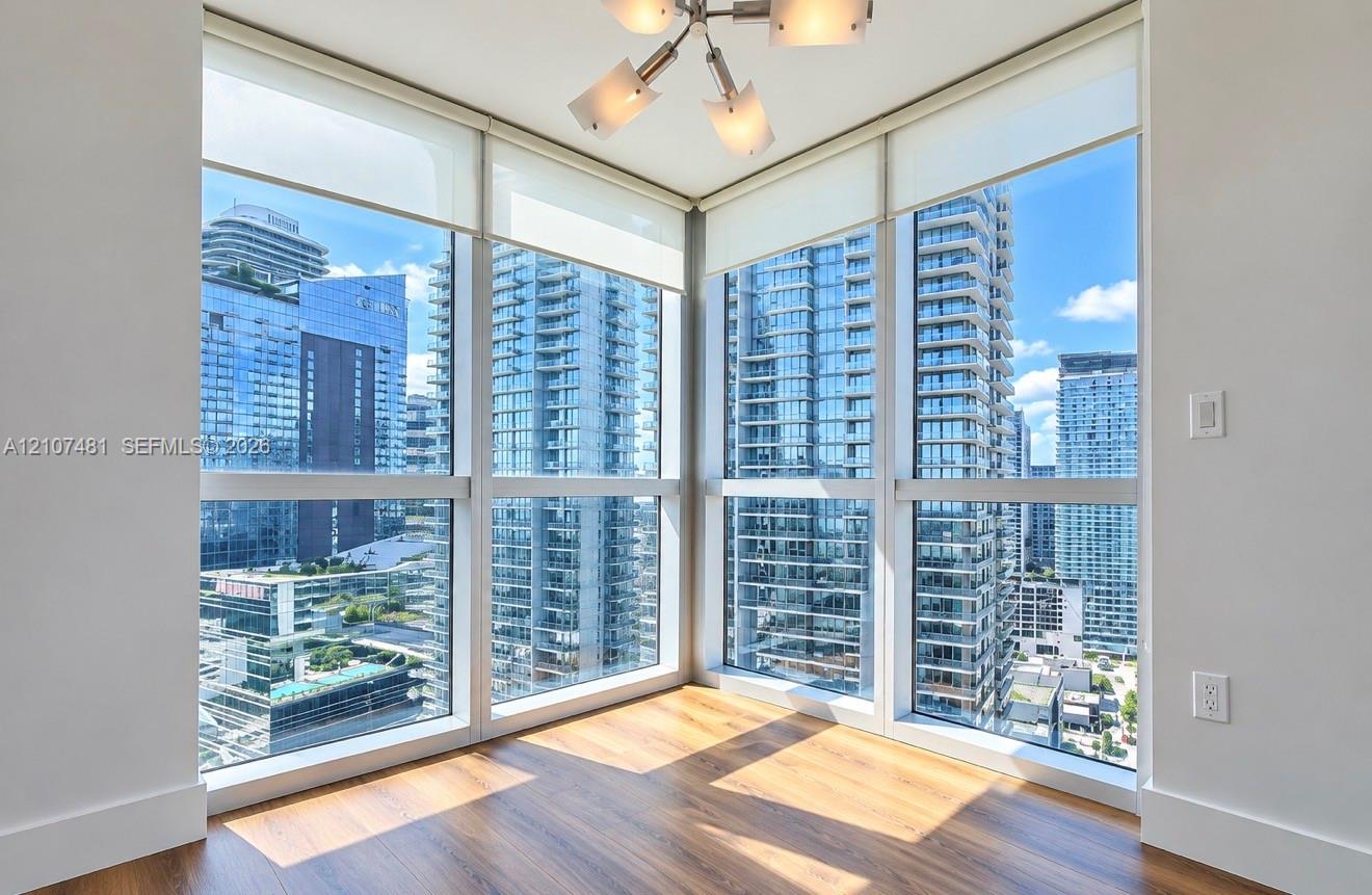 Floor-to-ceiling corner windows, wood-finish flooring, and a modern multi-arm light fixture
