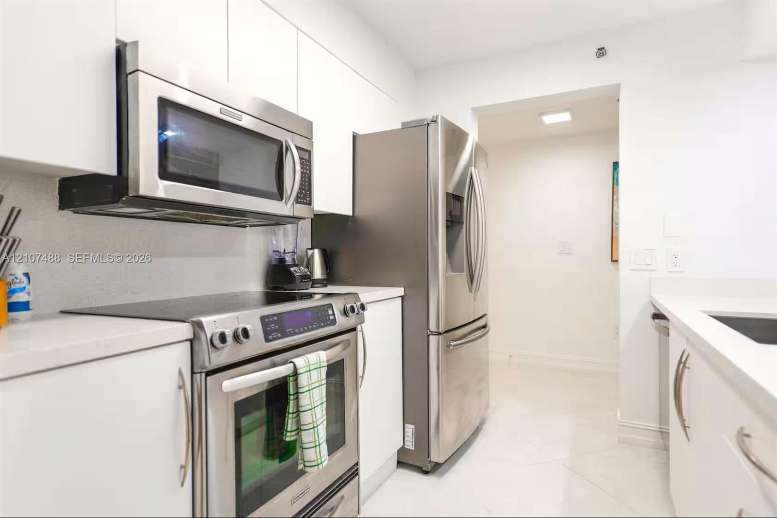Kitchen featuring sleek white flat-panel cabinetry, light-toned countertops, and stainless steel appliances, including an over-the-range microwave and a bottom-freezer refrigerator