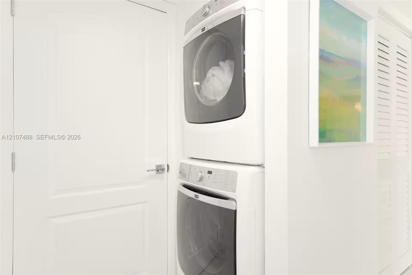 Stacked front-loading washer and dryer, solid core panel door with metallic hardware, and louvered closet door