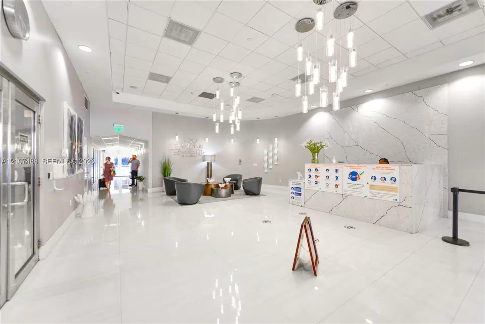 Lobby featuring high-gloss tile flooring, white stone-finish reception desk with dramatic veining, and modern multi-pendant lighting fixtures