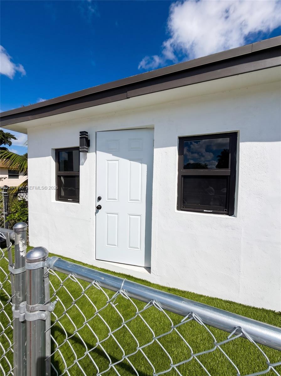Stucco exterior featuring a white paneled door, dark-toned window frames, and exterior wall-mounted lighting