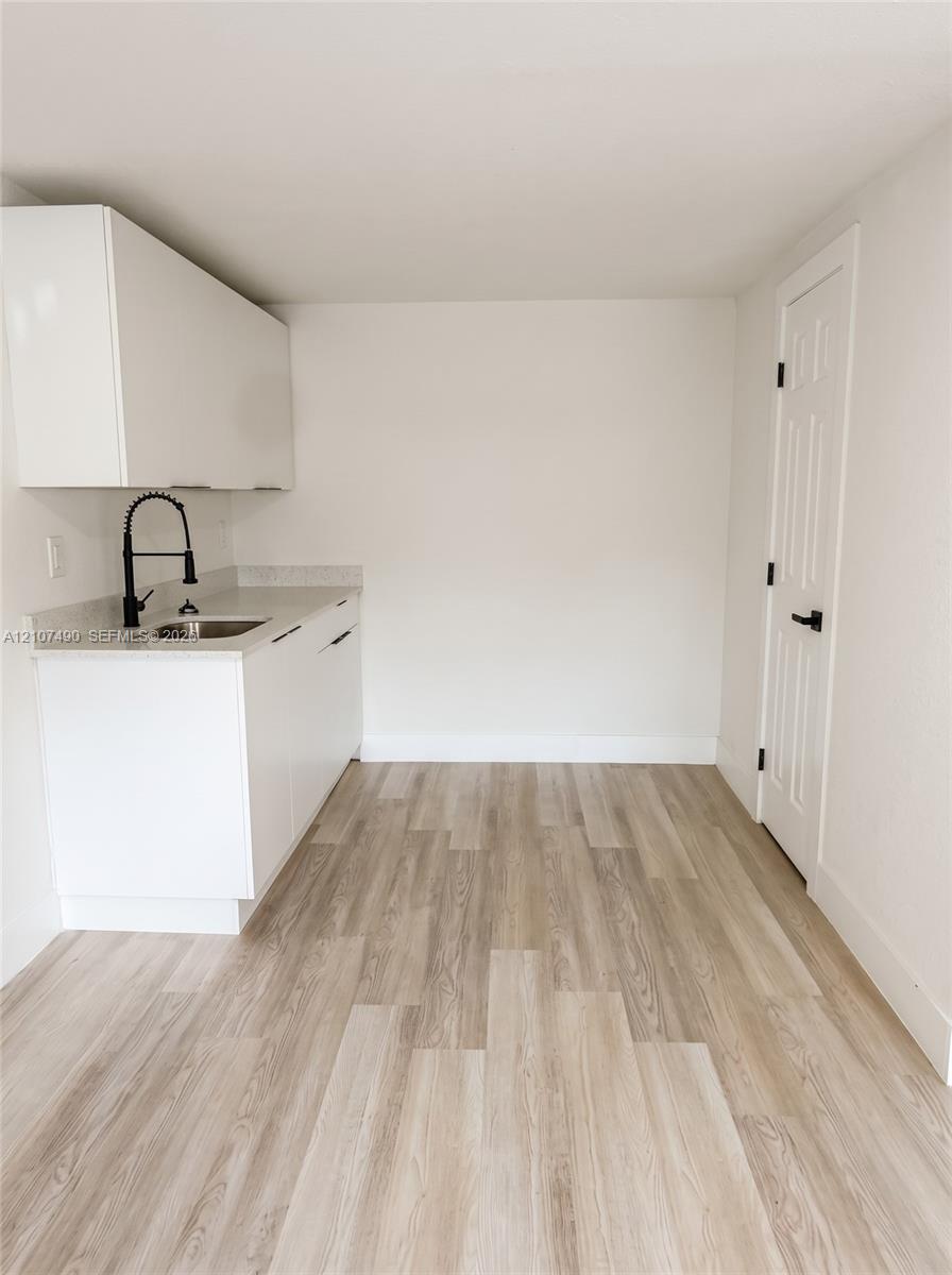 Sleek kitchenette featuring white flat-panel cabinetry, quartz countertops, an undermount sink with a matte black high-arch faucet, and wood-finish flooring