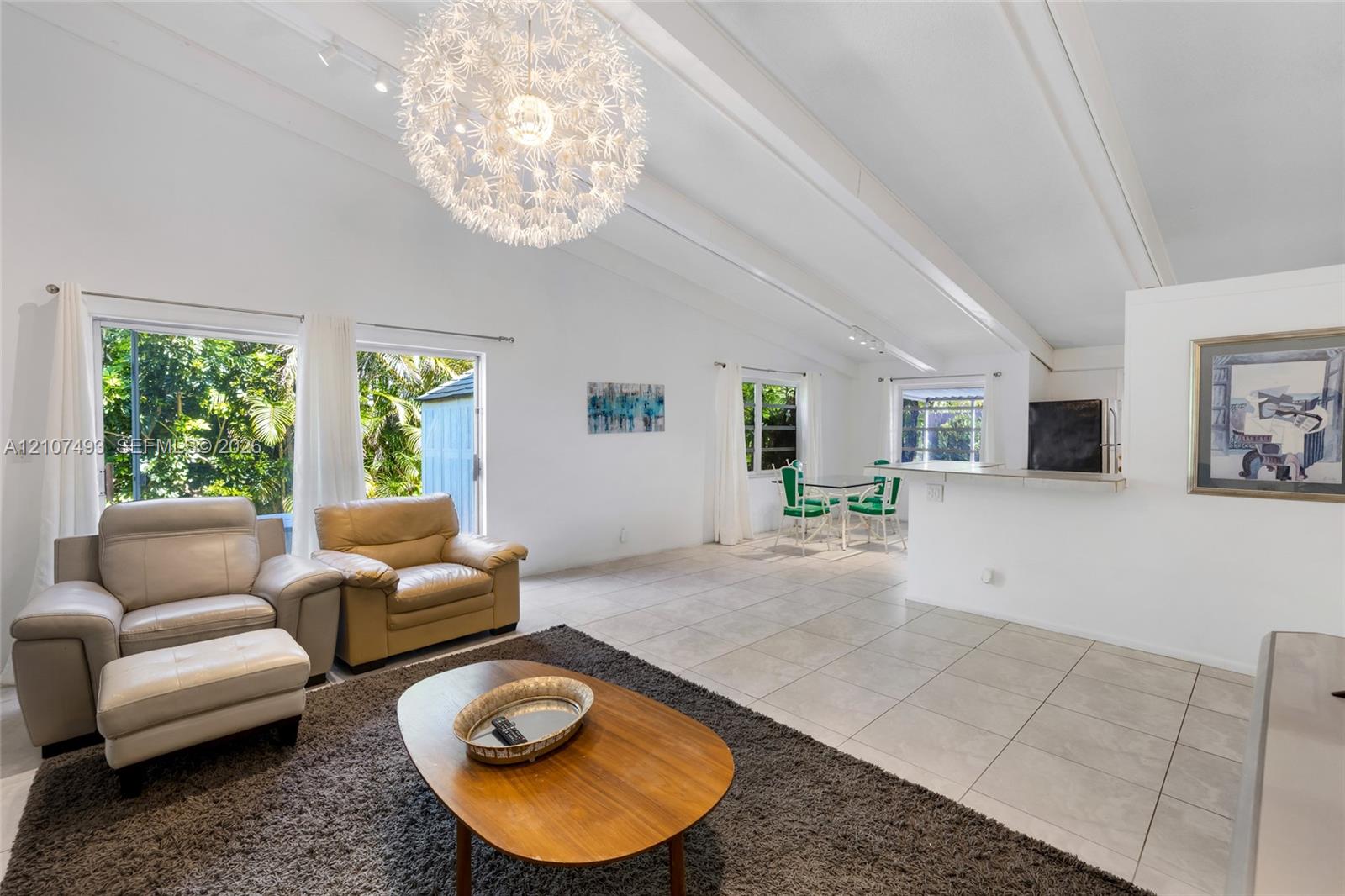 Vaulted ceilings with exposed beams, large-format tile flooring, oversized spherical pendant lighting, track lighting, and a breakfast bar counter
