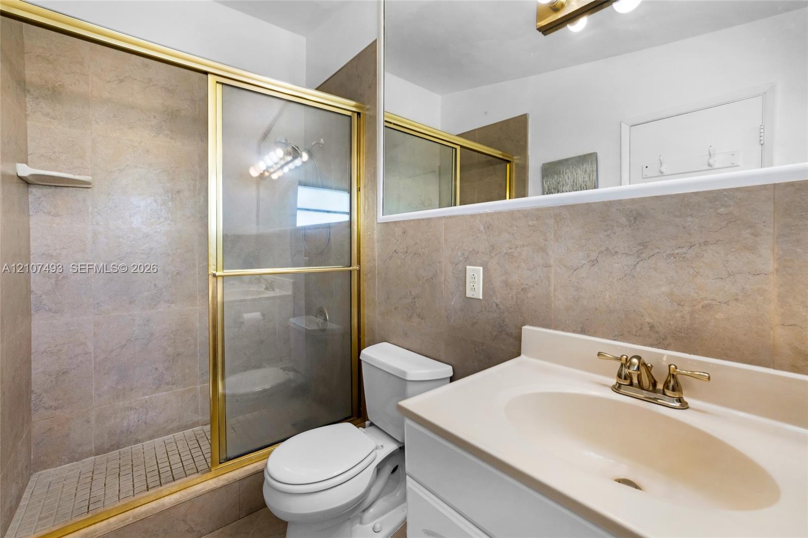 Bathroom featuring a shower stall with a glass door, tile surround, vanity with an integrated sink, and a wall-to-wall mirror