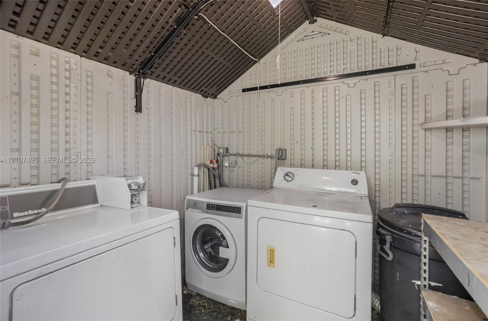 Utility structure featuring high-vaulted corrugated paneling, integrated wall-mounted shelving, and exposed electrical conduits