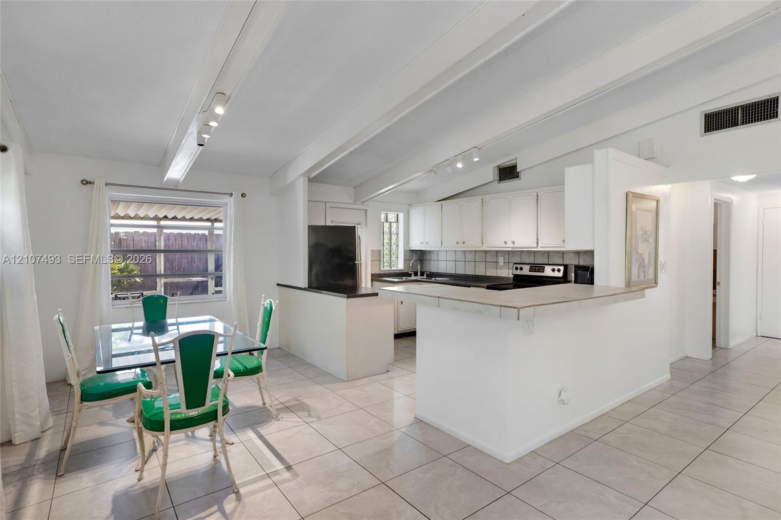Vaulted ceilings with exposed beams, tile flooring, breakfast bar, and track lighting