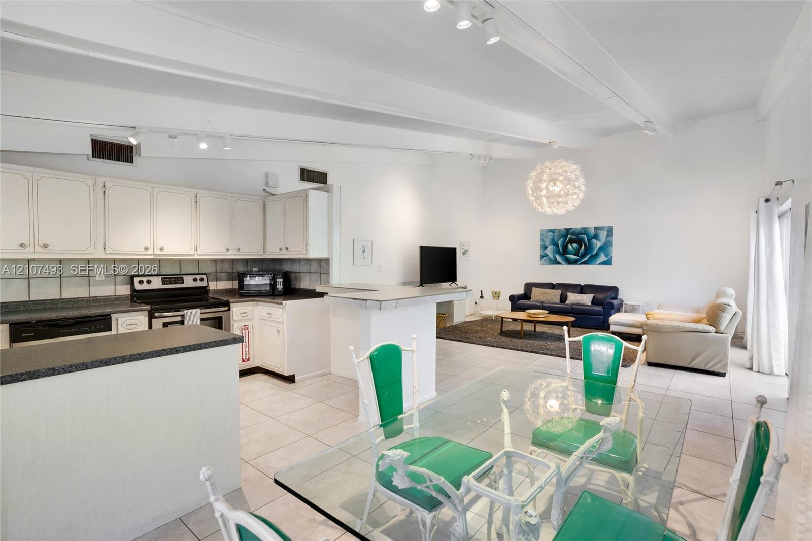 Open-concept interior featuring vaulted ceilings with exposed beams, ceramic tile flooring, a kitchen peninsula, and recessed lighting