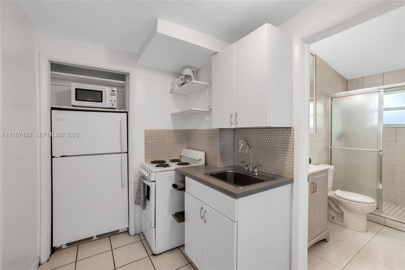 Kitchen featuring white cabinetry, solid-surface countertop, hexagonal tile backsplash, and ceramic tile flooring