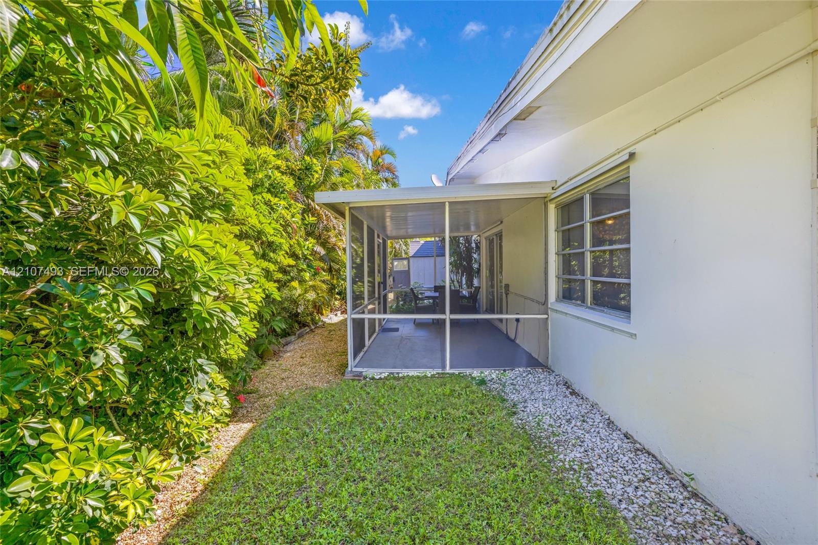 Screened-in patio with concrete flooring, manicured lawn, established perimeter hedges, and decorative rock landscaping