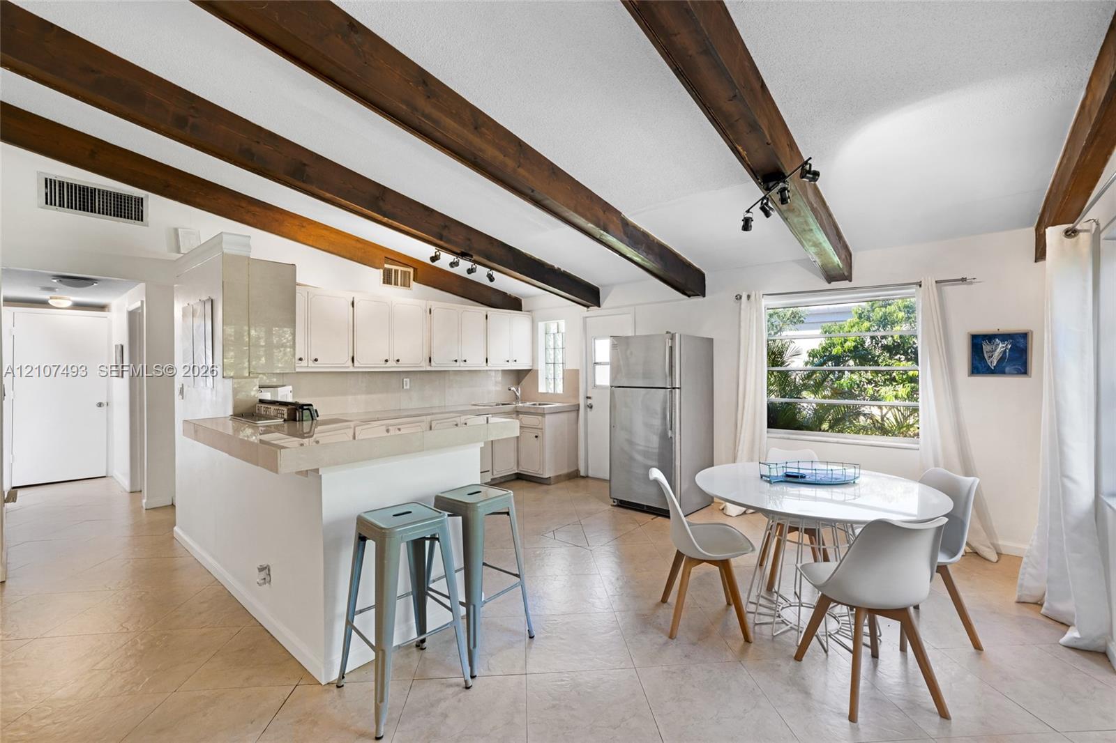 Exposed dark wood ceiling beams, tile flooring, white cabinetry, integrated peninsula, and track lighting