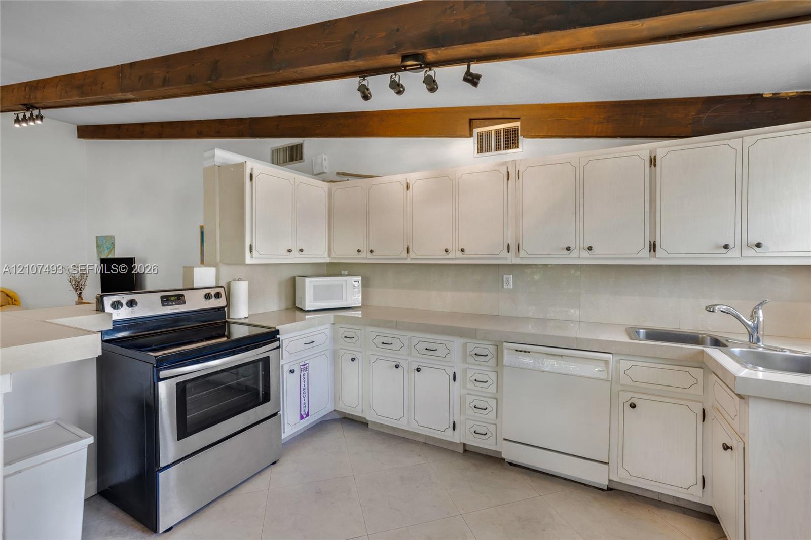 Kitchen featuring white cabinetry, solid-surface countertops, stainless steel range, integrated dishwasher, and exposed wood ceiling beams