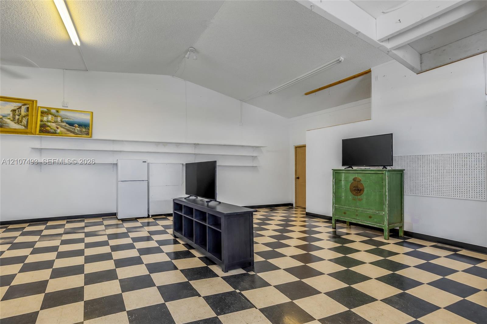 Interior space featuring vaulted ceilings, high-contrast checkerboard flooring, linear wall-mounted shelving, and integrated pegboard wall panels