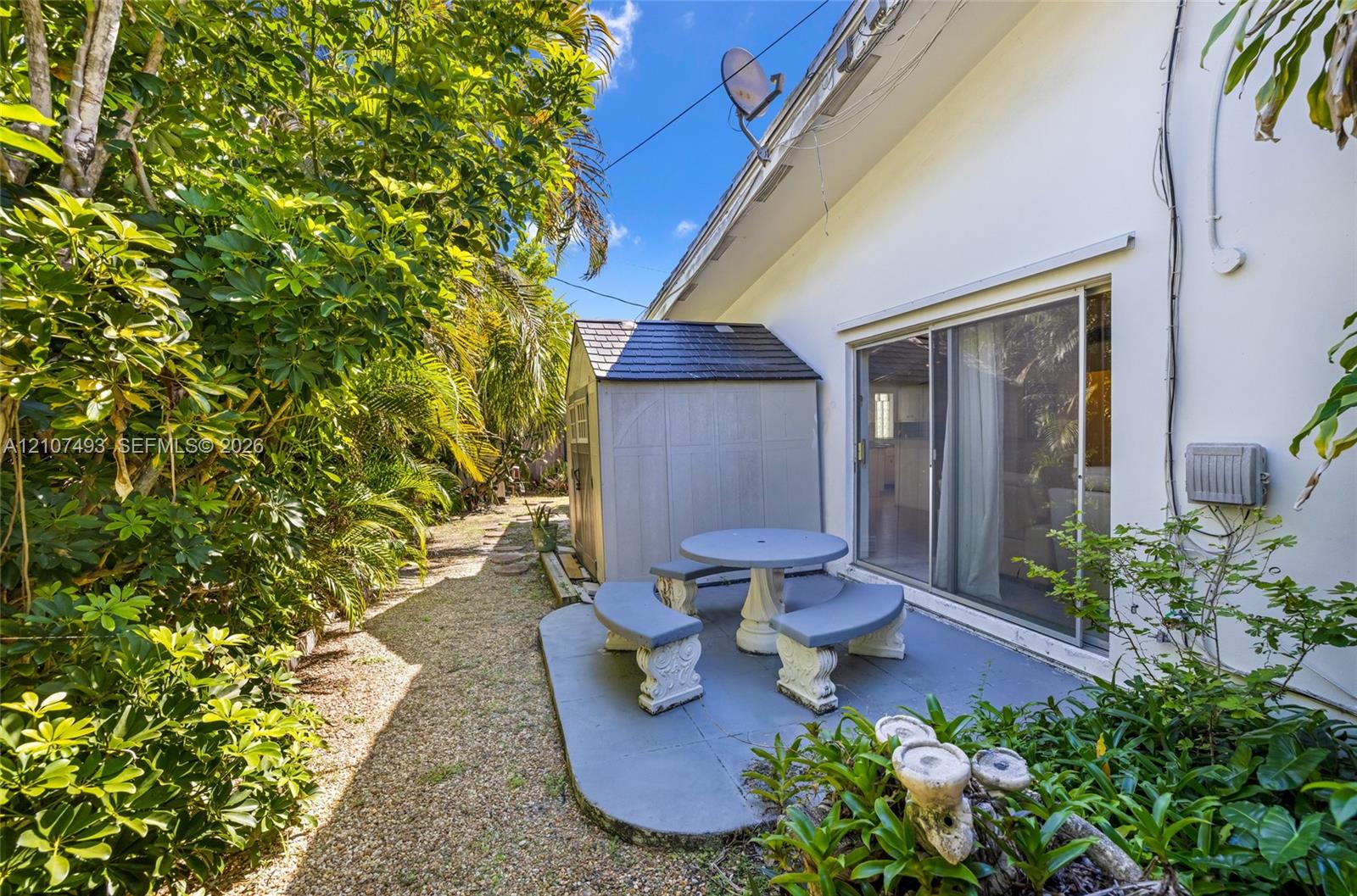 Side patio featuring a concrete slab, sliding glass door access, and a detached storage structure nestled among mature landscaping