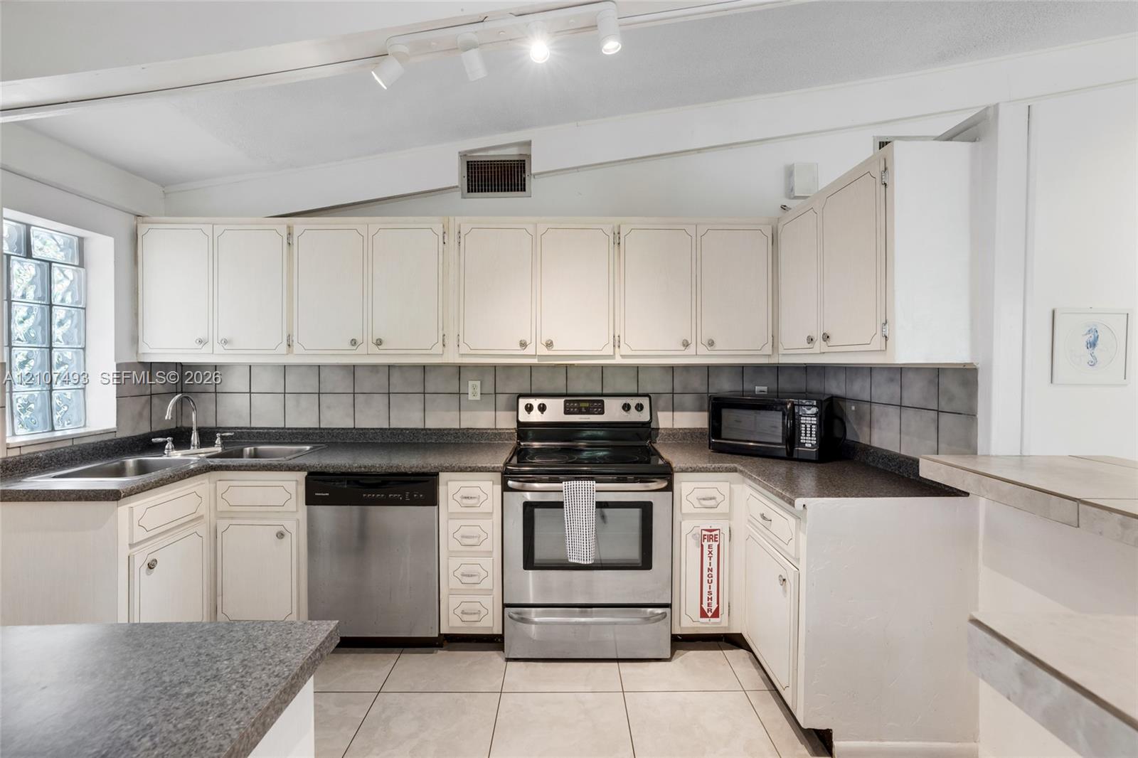 Kitchen featuring cabinetry with white shaker-style doors, stone-finish countertops, stainless steel appliances, ceramic tile backsplash, and ceramic floor tiling